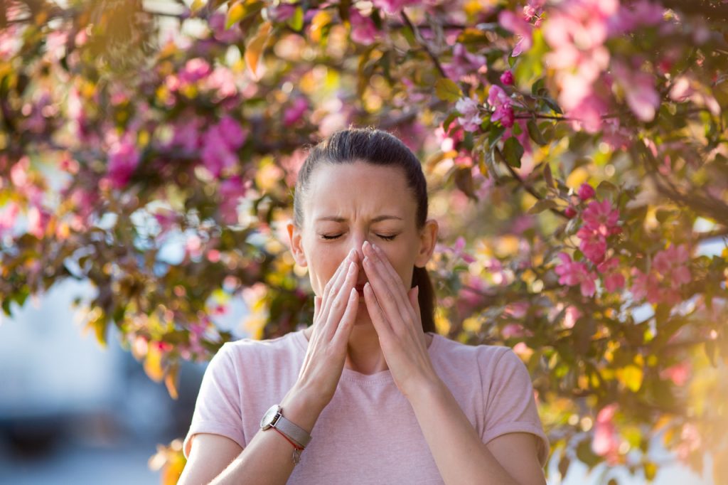 A person blowing their nose into a tissue, indicating allergy symptoms and the negative impact on quality of life.